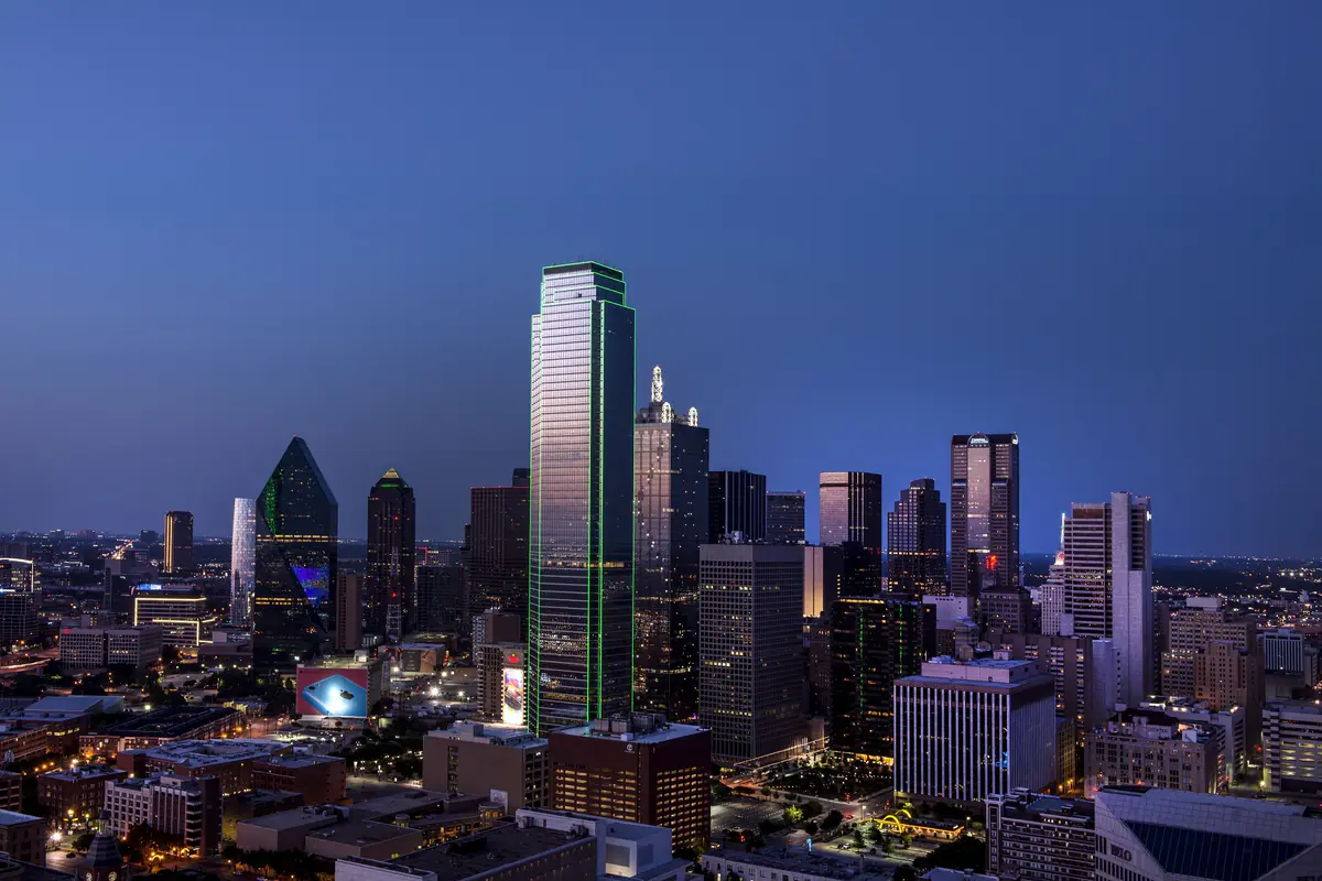 Downtown Dallas skyline illuminated at dusk beneath a blue sky